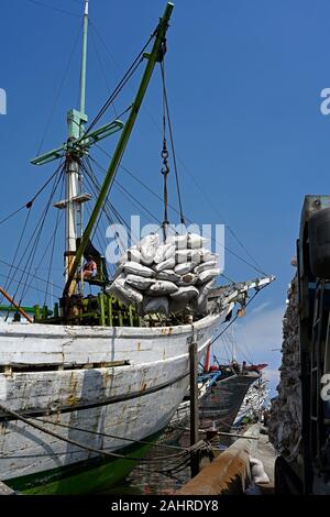 Jakarta, Indonesien - 2019.12.18: Entladung der Ware in Säcken aus Holz- prahu pinisi (kapal layar Motor klm) auf Lkw im Sunda Kelapa Hafen Stockfoto