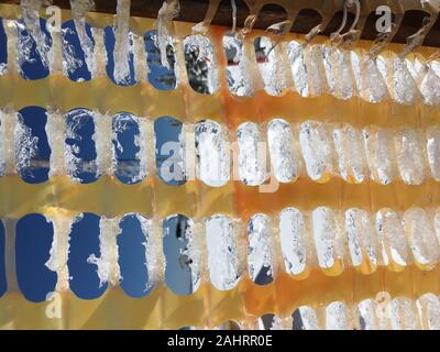 Gelb Kunststoff-beschichtete Zaun mit Eis und Raureif auf dem Hintergrund des blauen Himmels abgedeckt. Stockfoto