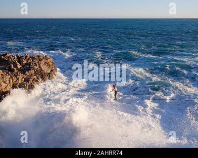 Junger Mann, der über großen Wellen auf einer felsigen Küste aufprallte. Cap de Nice, Französische Riviera, Alpes-Maritimes, Frankreich. Stockfoto