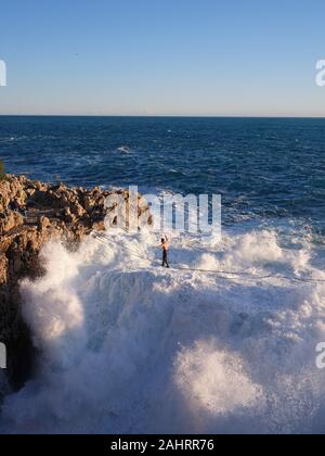 Junger Mann, der über großen Wellen auf einer felsigen Küste aufprallte. Cap de Nice, Französische Riviera, Alpes-Maritimes, Frankreich. Stockfoto