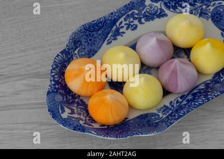 Baisers, verschiedene Farben, auf einem gemusterten blauen und weißen Platte. Graues Holz Hintergrund Stockfoto