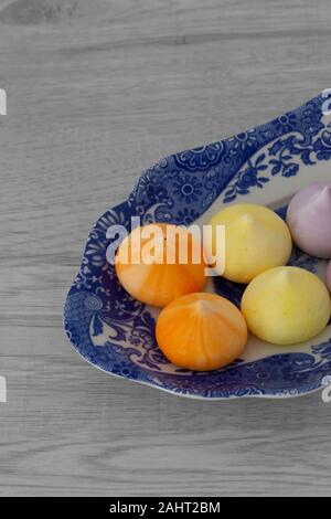 Baisers, verschiedene Farben, auf einem gemusterten blauen und weißen Platte. Graues Holz Hintergrund Stockfoto