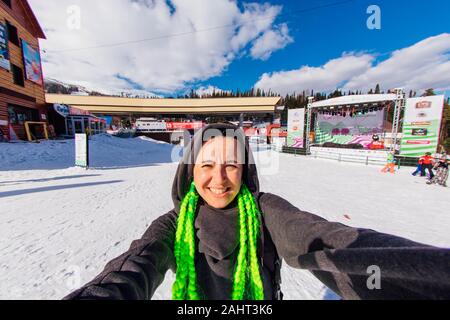 Sheregesh, Kemerovo Region, Russland - 09 April, 2019: Selfie portrait von jungen fröhliche Frau mit grünen Flechten auf einem schneebedeckten Hang im Winter Skigebiet. Stockfoto