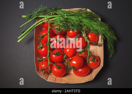 Red Cherry Tomaten mit Dill auf schwarzem Hintergrund in einem Karton. Stockfoto