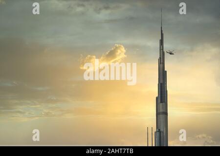 Burj Khalifa schließen oben mit bewölktem Himmel im Hintergrund und Hubschrauber in der Nähe der Turm fliegen. Sonnenuntergang Blick auf Burj Khalifa Stockfoto