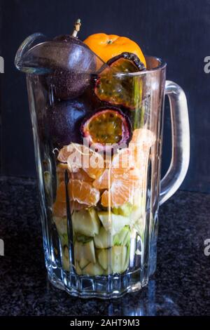 Verschiedene Arten von Früchten wie Passionsfrucht, Mandarinen und Äpfel in einem Glas Mug auf schwarzem Hintergrund Stockfoto