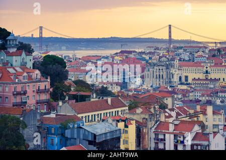 Lissabon Panoramablick. Bunte Wände der Gebäude von Lissabon, mit orangefarbenen Dächern und der 25. April Bridge im Hintergrund, bei Sonnenuntergang. Reisen Stockfoto