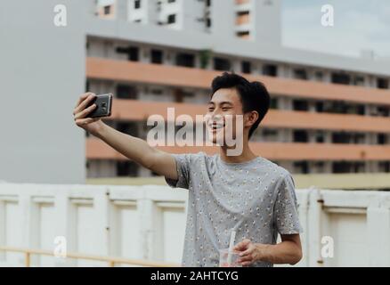 Asiatischer männlicher Vlogger, der authentische Chinatown, Singapur-Erfahrung mit Smartphone, HDB-Gehäuse im Hintergrund, Content Creator, Street Vlogging erfasst Stockfoto