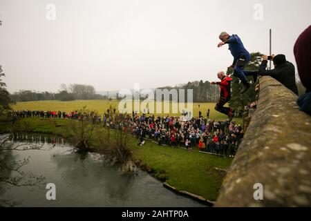 Eine Nächstenliebe, die Wettbewerber springt von der Okeover Brücke in den Fluss Dove während der mapleton raft Race und Brücke springen, in Mapleton, in der Nähe von Ashbourne, Derbyshire, als Teil der Tag des Neuen Jahres feiern. Stockfoto