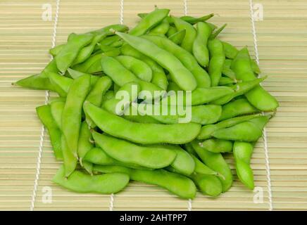 Stapel von gekochten edamame, grüne Sojabohnen, maodou, auf einem Bambus Matte. In Salzwasser gekochten Sojabohnen, Glycine max., eine reiche auf Protein Hülsenfrucht. Stockfoto