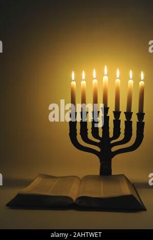 Menorah und offene Bibel mit 7 brennenden Kerzen auf goldenem Hintergrund isoliert. Vertikale erschossen. Stockfoto