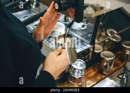 Nahaufnahme eines Barista vorbereiten Milch in eine Kaffeemaschine für Hinzufügen zu Kaffee. Stockfoto