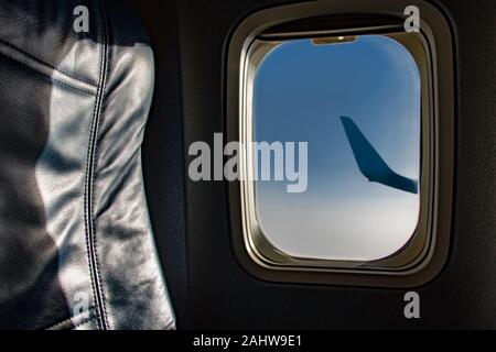 Eine leere Leder Stuhl im Flugzeug. Blau Sitz neben Fenster mit blauen Himmel in fliegenden Flugzeug. Stockfoto