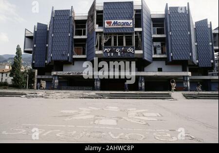 17. August 1993 während der Belagerung von Sarajevo: eine Shell - beschädigte Kaufhaus steht darüber hinaus die verschlissenen Symbol für die Olympischen Spiele von 1984, in der die Kinder von Sarajevo Square im Zentrum der Stadt gebaut. Stockfoto