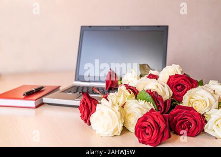 Blumen Geschenk frische weiße und rote Rosen am Arbeitsplatz auf leicht rosa Hintergrund. Auf hölzernen Tisch in der Nähe Laptop Tastatur ist groß Anzahl der Rosen. V Stockfoto