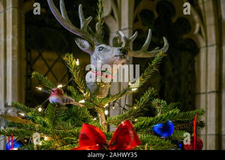 Einen echten Weihnachtsbaum, einfach dekoriert mit roten und blauen Kugeln und eine alternative Touch mit einer Hand aus papiermache Rentier Kopf gegeben ist, nach oben. Stockfoto