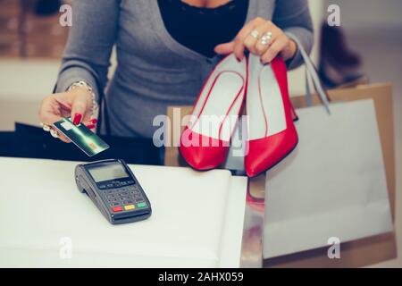 Zugeschnittenes Bild einer Frau Schuhe im Shop Kasse kauft, sie ist Zahlung mit einer Kreditkarte. Stockfoto