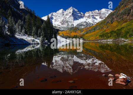 Maroon Bells Herbst Laub und Aspen Bäume im Schnee der Colorado Rocky Mountains und den See Reflexion über einen blauen Himmel Tag abgedeckt Stockfoto