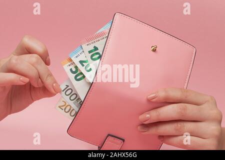 Rosa Geldbeutel und Euro-banknoten in weibliche Hände auf rosa Hintergrund. Geschäftskonzept und Instagram. Stockfoto