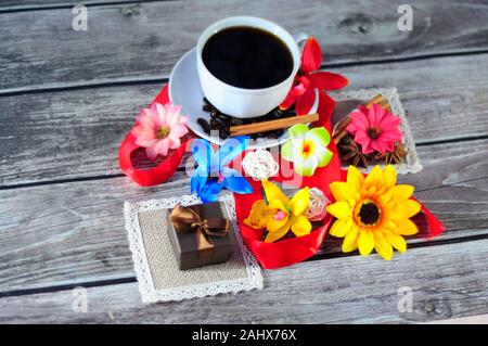 Eine weiße Keramik Tasse mit Kaffee auf eine Untertasse verziert mit Zimt und Anis, ein kleines Geschenk Box auf eine Serviette von blütenknospen umgeben. Close-up. Stockfoto