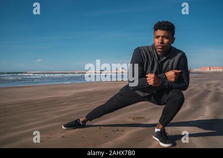 Porträt eines athletischen Mann Beine dehnen vor dem Training am Strand. Sport und gesunde Lebensweise. Stockfoto