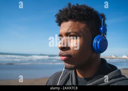 Porträt eines athletischen Mann Musik hören mit Kopfhörern beim Stillstehen für Übung am Strand. Sport und gesunde Lebensweise. Stockfoto