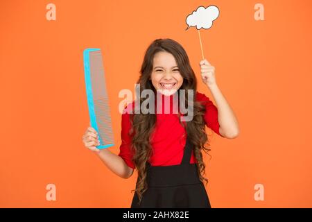 Äußerst effektive Produkt. Friseur für Kid. Schönheit Mode. Denken Sie über neue Frisur. Kid halten großen Kammaufsatz. Pflege und bürsten Sie Ihr Haar. Kleines Mädchen schöne lange Haare. Kind mit lockigem Haar. Stockfoto