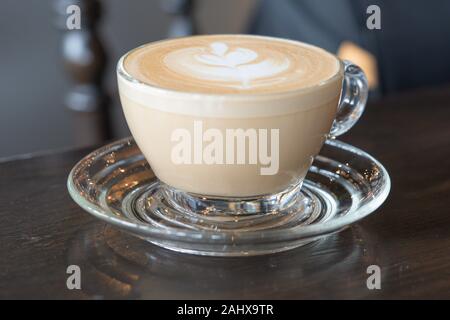 Cappuccino oder Latte Kaffee in ein klares Glas mit Herz auf Holz- Hintergrund Stockfoto