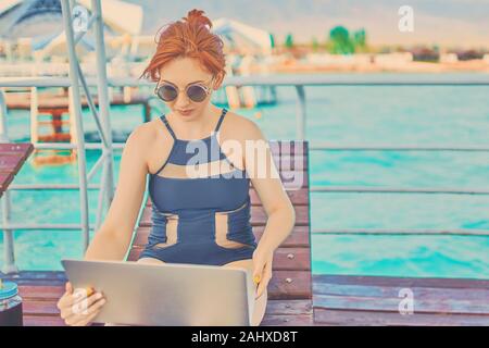 Frau arbeiten mit Laptop auf hölzernen Terrasse vor dem wunderschönen Meer, Urlaub in Urlaub mit der Natur im Sommer entspannen. Stockfoto