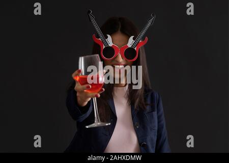 Junge Frau mit funky Brille und mit einem Glas Wein an Silvester Party. Stockfoto