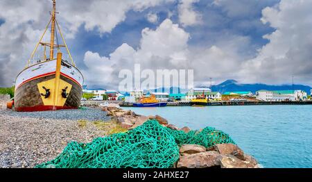 Eine kommerzielle Fischerei Hafen in einer kleinen Küstenstadt in Island, mit einem grünen Netz in den Vordergrund und einer alten hölzernen Schiff aus dem Wasser. Stockfoto