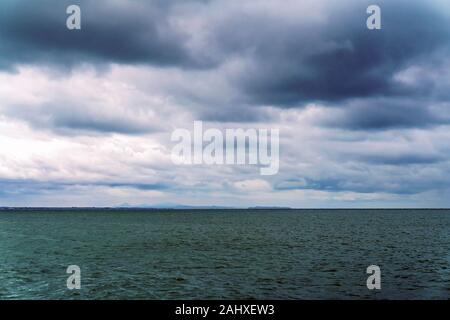 Licht regen verdeckt Vision und Erweichung der Landschaft als Sturm Wolken über dem Meer auf einem Stumpf und windigen Tag Stockfoto