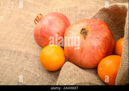 Zwei reife Granatäpfel und Mandarinen auf einem Hintergrund aus grobem Homespun Stoff close-up. Fitness Ernährung. Gesunde Ernährung Stockfoto