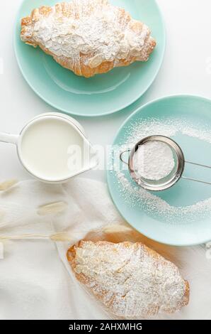 Croissants mit mandelflocken und Puderzucker auf Türkis Platte. Overhead, senkrecht. Frühstück Konzept Stockfoto