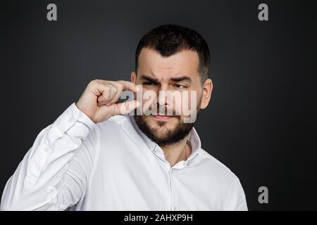 Gut aussehender bärtiger Mann mit zwei Händen vor Ihm zeigen geringe Größe auf schwarzem Hintergrund Stockfoto