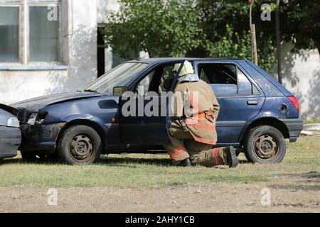 Feuerwehrmänner, die Teilnahme an einer Schulung, wo sie Feuer aus einem Auto Löschen in einem anderen Fahrzeug zusammengestoßen. Feuerwehrmann untersucht die zerschmetterte Auto. Stockfoto