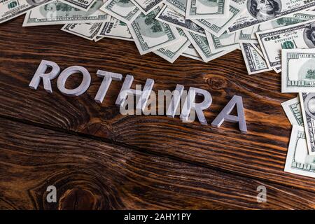 Wörter ROTH IRA auf Holzfläche mit Metallbuchstaben gelegt Und US-Dollar-Banknoten Stockfoto