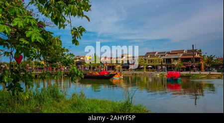 Hoi An, Vietnam. Mai 05, 2019: Traditionelle Holz- Boot auf dem Thu Bon Fluss mit alten gelben Gebäude in der Altstadt. UNESCO-Weltkulturerbe. Stockfoto