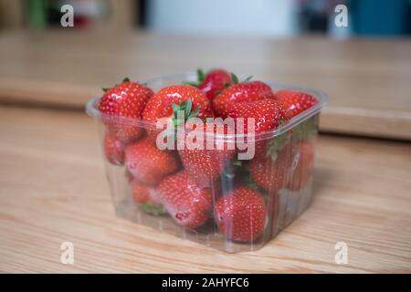 Kunststoff punnet von Erdbeeren auf einem Holztisch. Nahaufnahme und verschwommenen Hintergrund. Köstliche frische rote Früchte. Nicht umweltfreundlich. Recycling zu tun. Stockfoto