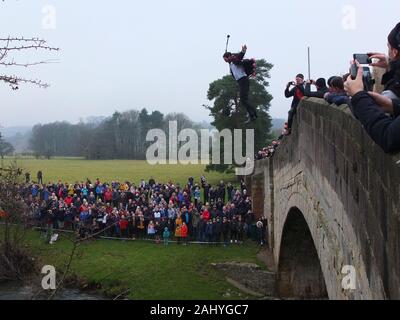 Mappleton (Mapleton) Brücke springen, jährlichen Tag der neuen Jahre Benutzerdefiniert. Teilnehmer im Anzug mit selfie Stick springt von okeover Brücke und in Fluss Dove. Stockfoto