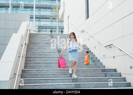 Freundliche asiatische Frau gehen Treppen mit bunten Shop Pakete. Shopping und Mode Konzept Stockfoto