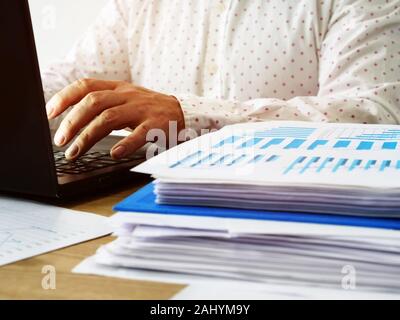 Ein junger Mann, ist das Schreiben auf einem Laptop Tastatur in einem Büro. Jahresbericht schreiben. Stockfoto