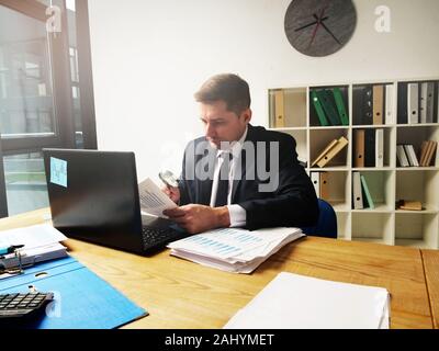Buchhalter arbeitet in einem Büro mit Papieren und einer Lupe. Überprüfung der Berichte und Jahresabschlüsse. Stockfoto