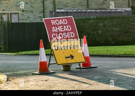 Eine rote Straße Schliessen Zeichen (UK) in der Mitte der roten und weißen Leitkegel. Eine gelbe Abzweigung Zeichen ist darunter. Stockfoto