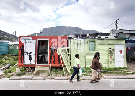 Südafrika: Township Imizamo Yethu in den Vororten von Hout Bay, in der Nähe von Cape Town, Western Cape. Frauen gehen in eine Straße und Gemeinschaft Handy shop Stockfoto
