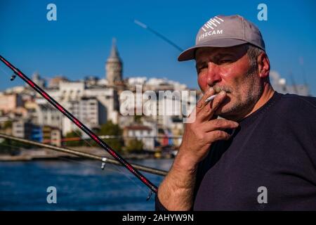 Ein Fischer ist das Rauchen einer Zigarette auf der Galata-brücke, Galata Köprüsü, dem Vorort Karaköy mit der Galata Turm, Galata Kulesi über den Bosporus gesehen Stockfoto