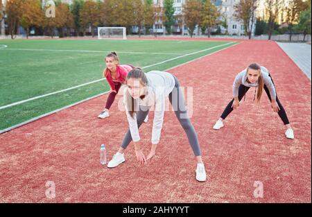 Positive Frauen Sport Übungen.. Die Gruppe der drei schöne junge Frauen, die Sport im sonnigen Tag im Park. Stockfoto