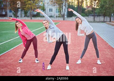 Positive Frauen Sport Übungen.. Die Gruppe der drei schöne junge Frauen, die Sport im sonnigen Tag im Park. Stockfoto