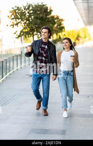 Lächelndes Paar im Herbst Outfit, Hände halten, bei jedem anderen suchen und gehen auf die Straße mit Einweg Kaffeetassen Stockfoto