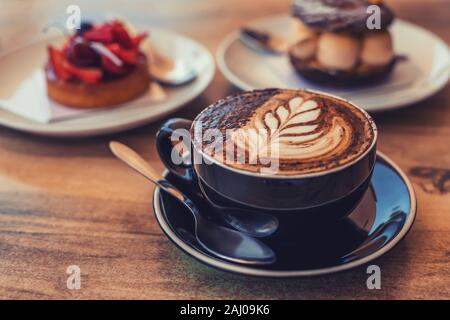 Eine Tasse Kaffee mit Kunst auf einem Tisch, verschwommenes Wüsten auf dem Hintergrund, getönt Stockfoto